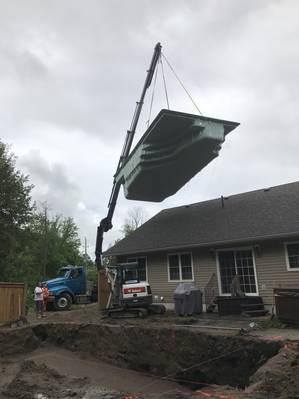 Crane lifting a fiberglass pool over a house in Barrie, Ontario